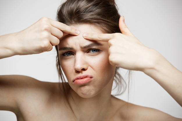 Jeune fille brune mécontente de son problème de peau de visage d'acné sur fond blanc. Cosmétologie de la santé et soins de la peau.