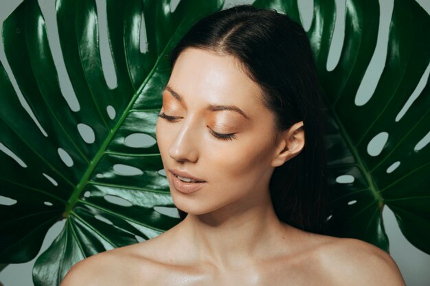Jeune fille brune posant avec des feuilles exotiques