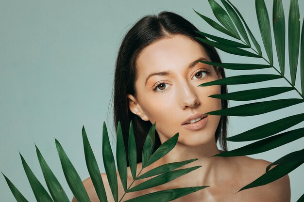 Jeune fille brune posant avec des feuilles exotiques