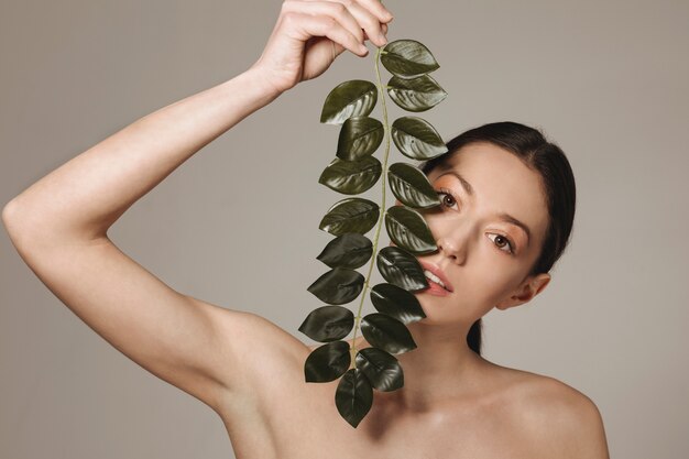 Jeune fille brune posant avec des feuilles exotiques