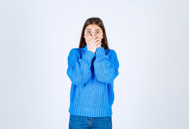 Jeune fille brune en pull bleu coning sa bouche sur blanc.