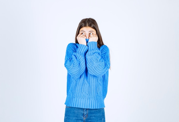 Jeune fille brune en pull bleu coning son visage sur blanc.