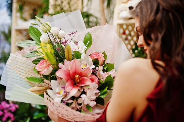 Jeune fille brune en rouge acheter des fleurs au magasin de fleurs