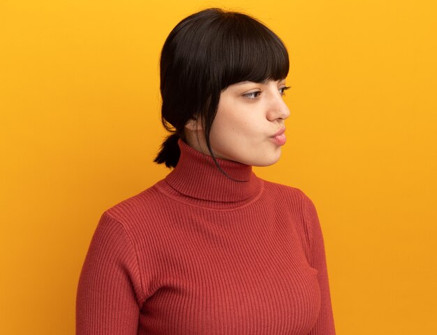 Une jeune fille caucasienne brune confuse regarde le côté isolé sur un mur orange avec un espace pour copie