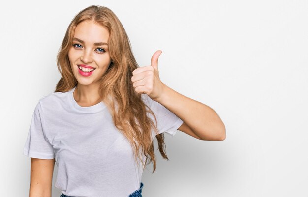 Jeune fille caucasienne portant un t-shirt blanc décontracté souriant heureux et positif, pouce vers le haut faisant un excellent signe d'approbation