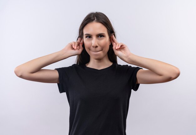 Jeune fille caucasienne portant un t-shirt noir a mis ses doigts autour des oreilles sur un mur blanc isolé