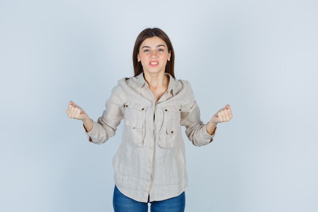 Jeune fille en chemise beige, jeans serrant les poings et semblant agitée, vue de face.