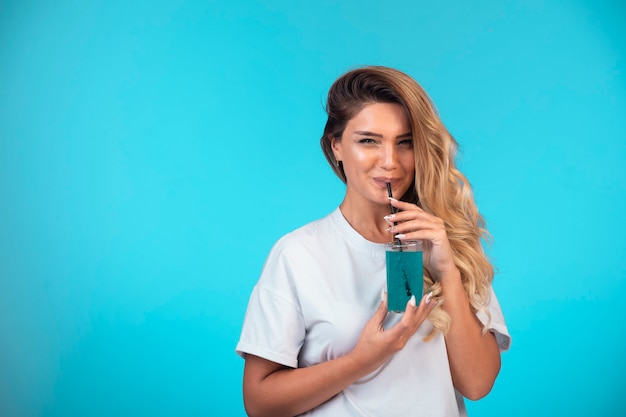 Jeune fille en chemise blanche buvant un verre de cocktail bleu.