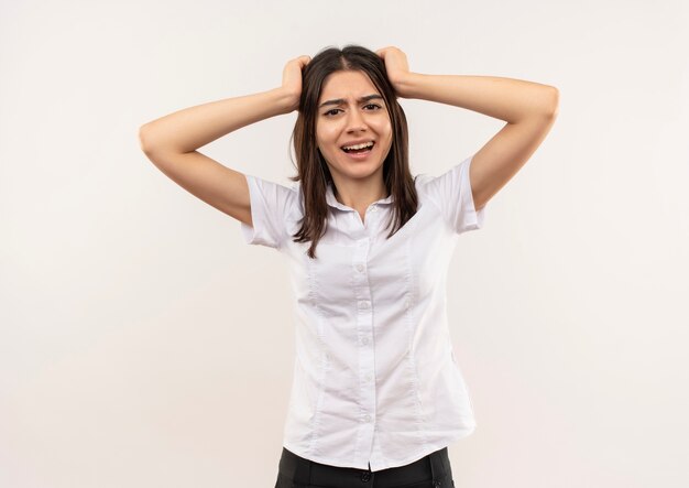 Jeune fille en chemise blanche se déchaîne en tirant ses cheveux debout sur un mur blanc