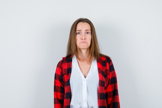 Jeune fille en chemise à carreaux, chemisier courbant les lèvres inférieures et semblant lésée, vue de face.