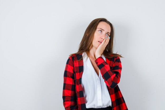 Jeune fille en chemise à carreaux, chemisier la joue appuyée sur la paume et l'air fatigué, vue de face.