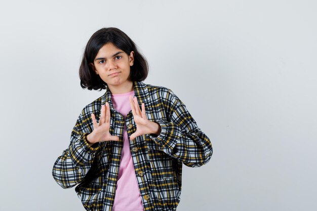 Jeune fille en chemise à carreaux et t-shirt rose étirant les mains comme tenant quelque chose et ayant l'air mignon, vue de face.