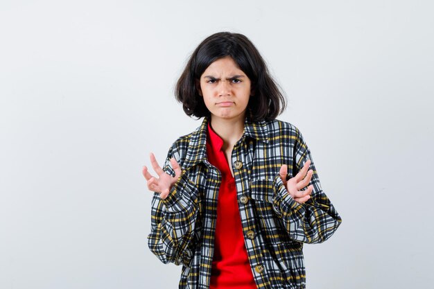 Jeune fille en chemise à carreaux et t-shirt rouge étirant les mains comme recevant quelque chose et ayant l'air en colère, vue de face.
