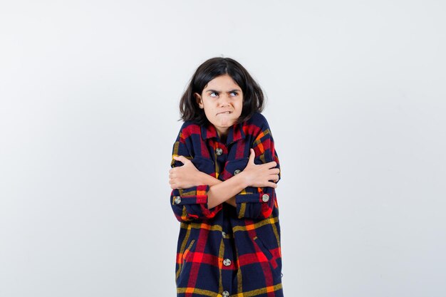 Jeune fille en chemise à carreaux tremblant de froid, mordant les lèvres et semblant harcelée, vue de face.