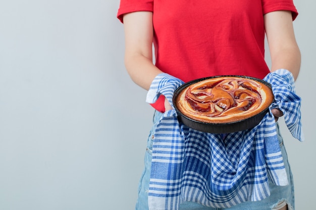 Jeune fille en chemise rouge tenant une tarte dans une casserole noire