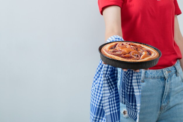 Jeune fille en chemise rouge tenant une tarte dans une casserole noire