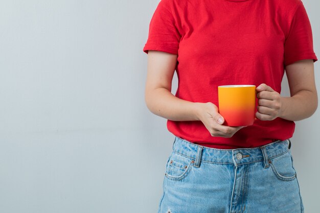 Jeune fille en chemise rouge tenant une tasse de boisson jaune