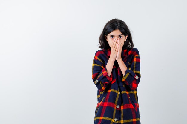 Jeune fille couvrant la bouche avec les mains en chemise à carreaux et l'air anxieux. vue de face.