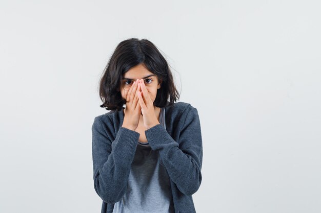 Jeune fille couvrant la bouche avec les mains en t-shirt gris clair et sweat à capuche zippé gris foncé et à la sérieuse