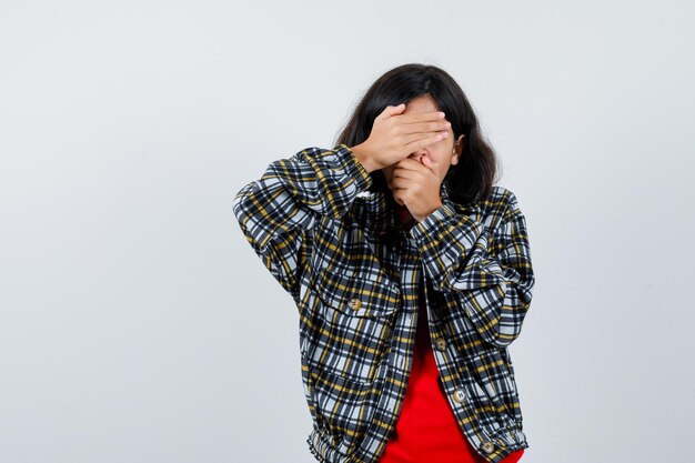 Jeune fille couvrant les yeux et la bouche avec les mains en chemise à carreaux et t-shirt rouge et l'air sérieux, vue de face.