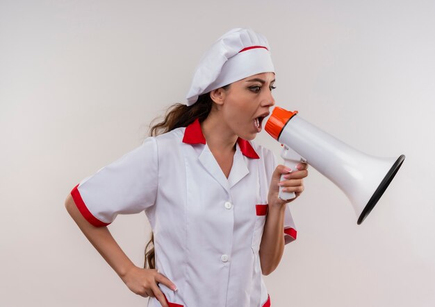 Jeune fille de cuisinier caucasien anxieux en uniforme de chef crie par haut-parleur isolé sur fond blanc avec espace copie