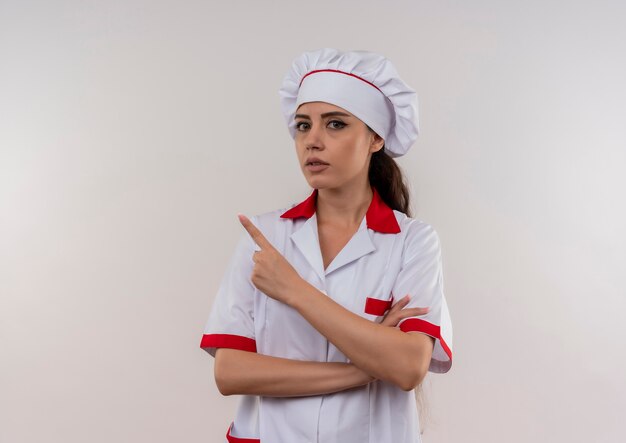 Jeune fille de cuisinier caucasien anxieux en uniforme de chef pointe vers le côté isolé sur fond blanc avec espace copie