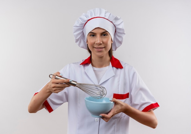 Jeune fille de cuisinier caucasien confiant en uniforme de chef détient un fouet et un bol sur blanc avec copie espace