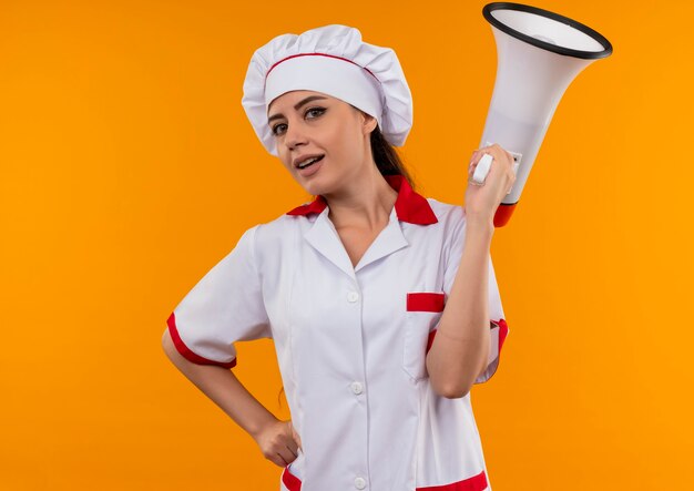 Jeune fille de cuisinier caucasien confiant en uniforme de chef détient haut-parleur isolé sur mur orange avec espace copie