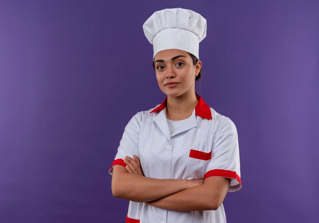 Jeune fille de cuisinier caucasien confiant en uniforme de chef traverse les bras et regarde la caméra isolée sur mur violet avec espace copie