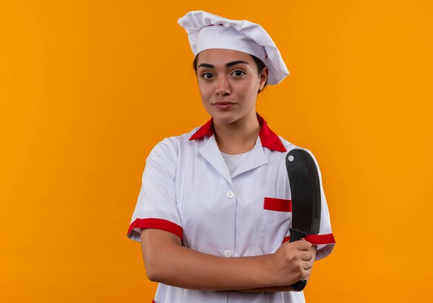 Jeune fille de cuisinier caucasien heureux en uniforme de chef tient un couteau isolé sur un mur orange avec copie espace