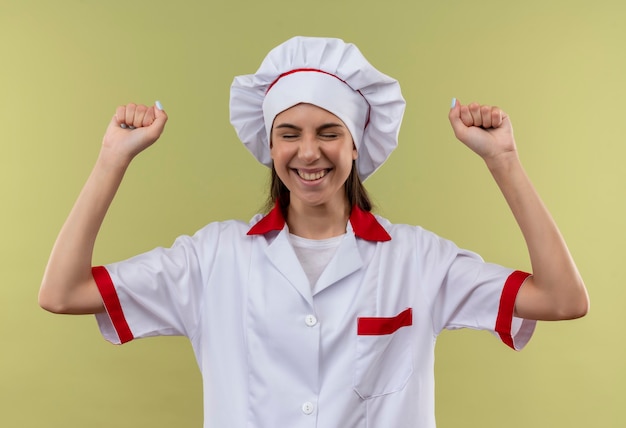 Jeune fille de cuisinier caucasien joyeux en uniforme de chef lève les poings isolé sur fond vert avec espace de copie