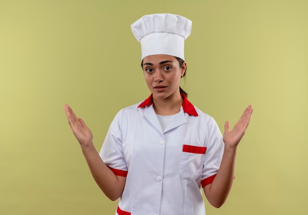 Photo gratuite jeune fille de cuisinier caucasien surpris en uniforme de chef tient les mains isolé sur un mur vert avec espace copie