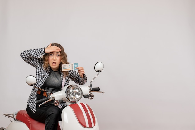 Jeune fille sur un cyclomoteur tenant un ticket en regardant quelque chose sur le gris