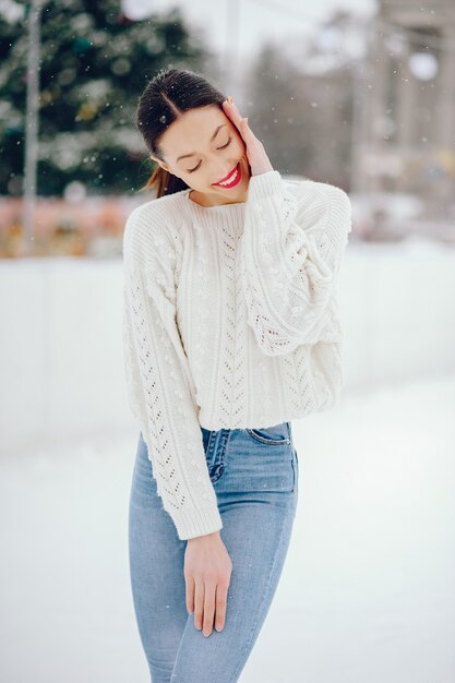 Jeune fille dans un pull blanc, debout dans un parc d'hiver