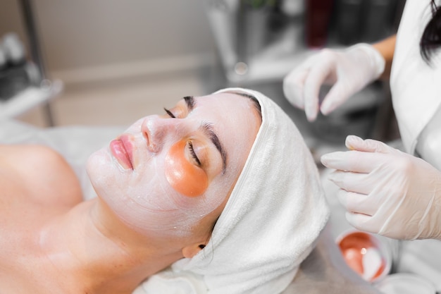 Une jeune fille dans un salon de beauté dans une salle de cosmétologie se trouve sur un lit se détend avec un masque sur son visage et des taches sous ses yeux