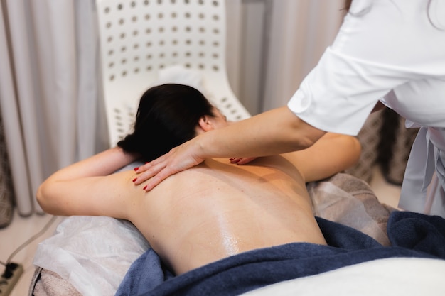 La jeune fille dans le salon spa reçoit un massage du dos et de la nuque, se trouve dans la table de cosmétologie, détendue et apprécie le processus