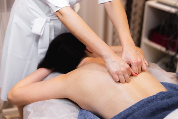 La jeune fille dans le salon spa reçoit un massage du dos et de la nuque, se trouve dans la table de cosmétologie, détendue et apprécie le processus