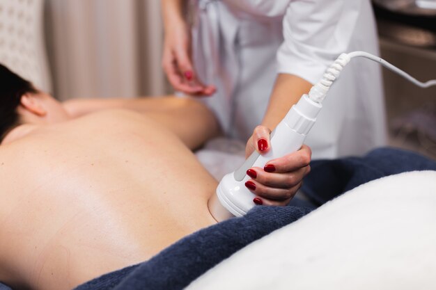 La jeune fille dans le salon spa reçoit un massage du dos et de la nuque, se trouve dans la table de cosmétologie, détendue et apprécie le processus