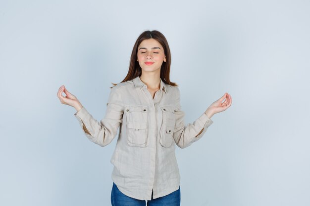 Jeune fille debout dans une pose de méditation en chemise beige, jeans et l'air paisible. vue de face.