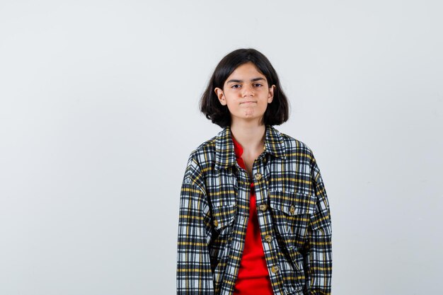 Jeune fille debout droite et posant à la caméra en chemise à carreaux et t-shirt rouge et l'air optimiste. vue de face.