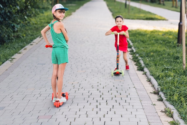 Jeune fille debout sur un scooter électrique avec son amie sur une passerelle dans le parc