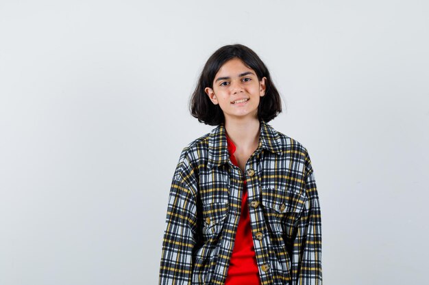 Jeune fille debout tout droit et se présentant à la caméra en chemise à carreaux et t-shirt rouge et l'air heureux. vue de face.