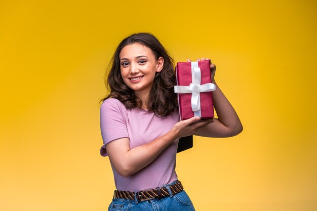 Jeune fille démontrant sa boîte-cadeau sur un mur jaune.