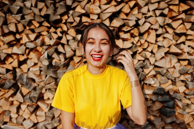 Photo gratuite jeune fille drôle avec des vêtements de maquillage lumineux sur une chemise jaune sur fond de bois