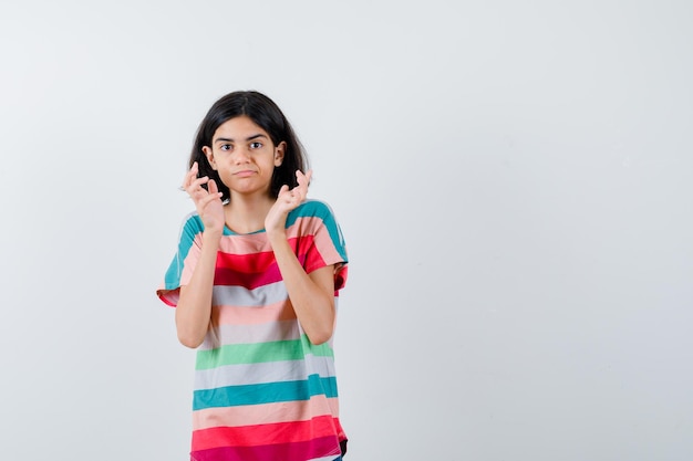 Jeune fille écartant les paumes en t-shirt à rayures colorées et semblant mignonne, vue de face.