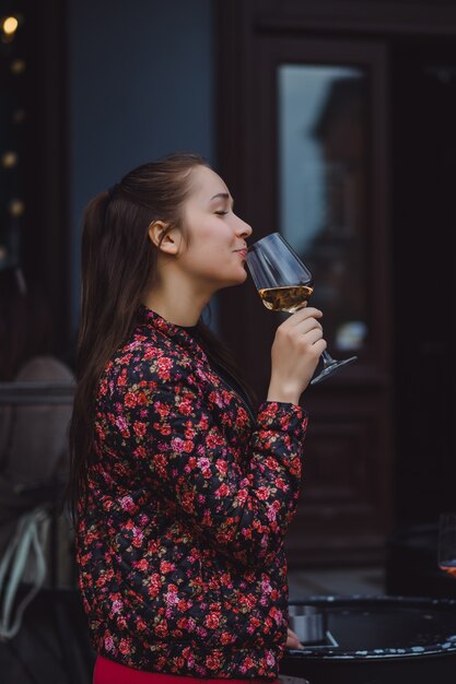 Une jeune fille élégante boit du vin dans un café de rue sur une terrasse d&#39;été. Une fille aux cheveux longs apprécie un verre de vin sur une soirée d&#39;été. Portrait. fermer