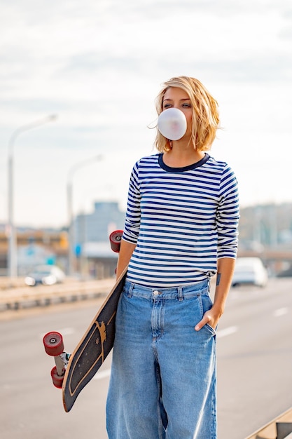 Jeune fille élégante urbaine marchant avec planche à roulettes. Portrait extérieur d'un modèle de femme sportive active. Mode de vie sain. Sports extrêmes. Look de mode, portrait de hipster en plein air. Portrait en gros plan d'un joli