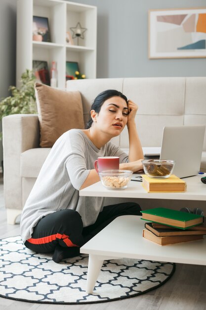 Jeune fille endormie assise sur le sol derrière une table basse dans le salon