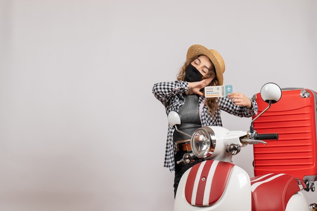 Jeune fille endormie avec un masque noir tenant un ticket debout près d'un cyclomoteur rouge