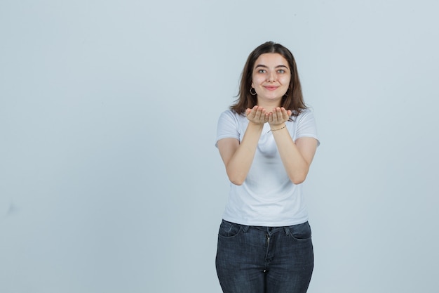 Jeune fille envoyant un baiser avec les mains en t-shirt, jeans et à la jolie. vue de face.